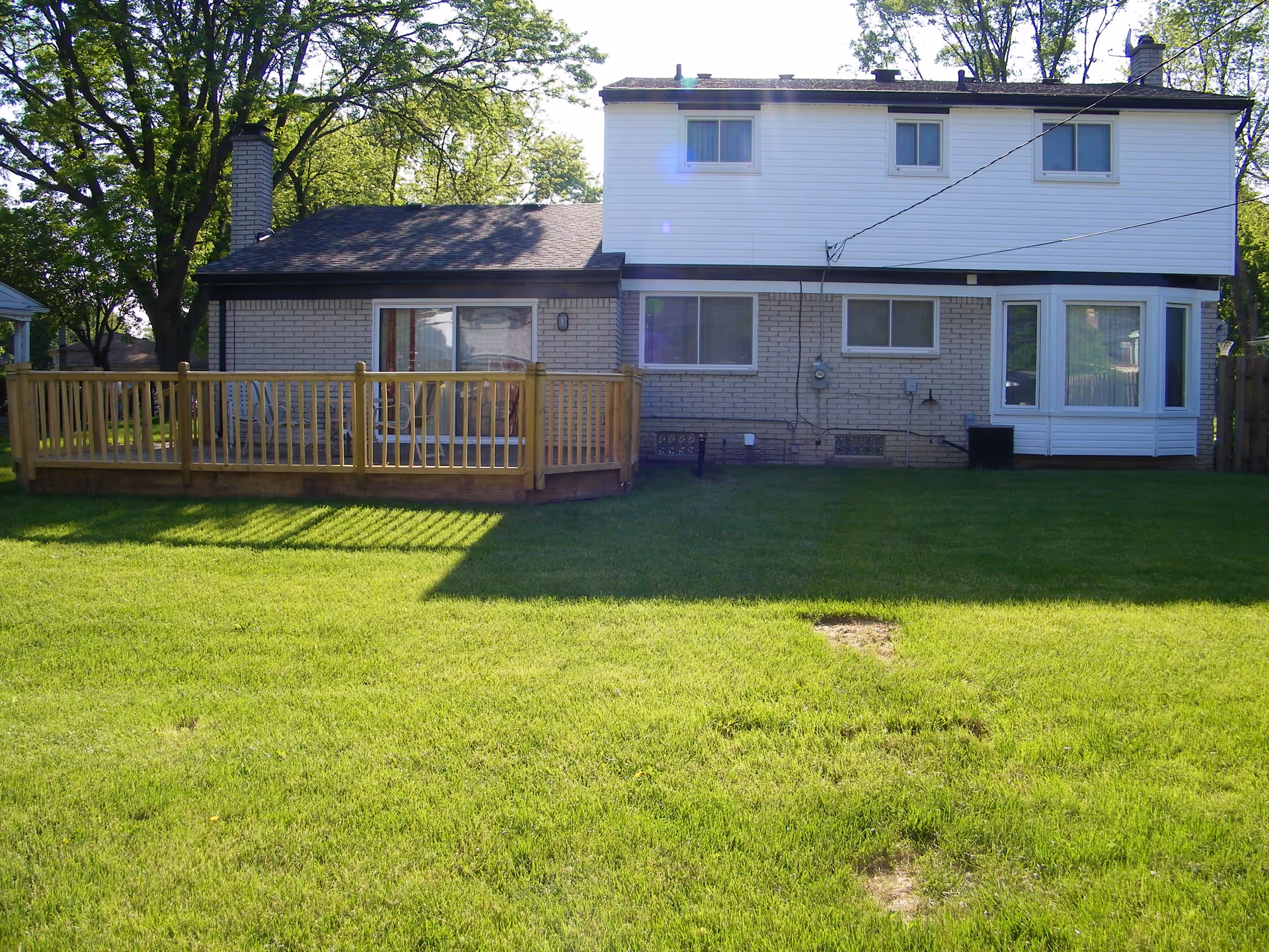 Rear exterior of a two-story house with a wooden deck and a green lawn.