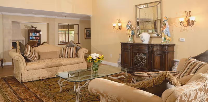 Elegant living room with beige sofas, a glass coffee table, patterned rug and a wooden sideboard with decorative items.