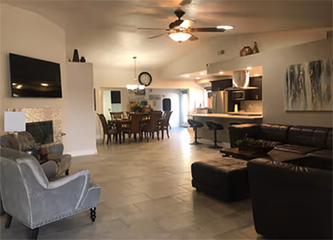 Open-concept living area with a leather sectional, armchairs, fireplace, dining table and kitchen with bar stools.