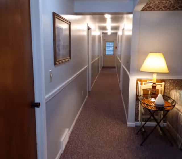 Long hallway inside a senior living facility with a side table and lamp on the right.
