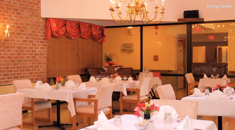 Formal dining room with tables set with white tablecloths, folded napkins, glassware and floral centerpieces.