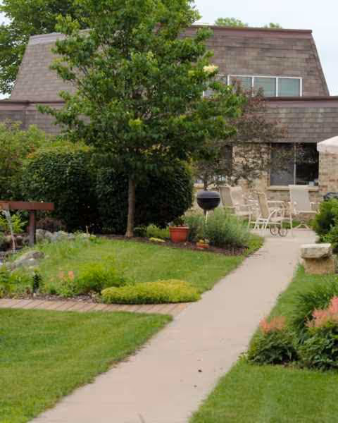 A landscaped courtyard path leads to a stone building with outdoor seating.