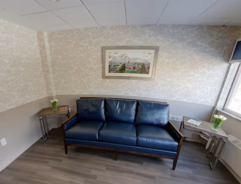 Navy blue leather sofa against a patterned wall with framed artwork and side tables holding vases of tulips in a small sitting area.