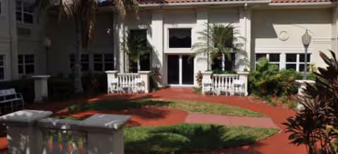 Front entrance of a Brookdale Deer Creek building with a red curved walkway and palm trees.