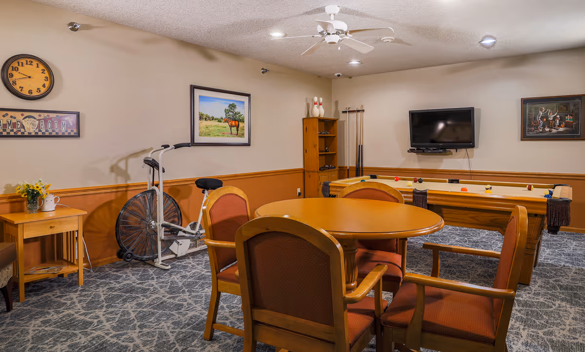 Activity room with a round table and chairs, a pool table, wall-mounted TV, and an exercise bike.