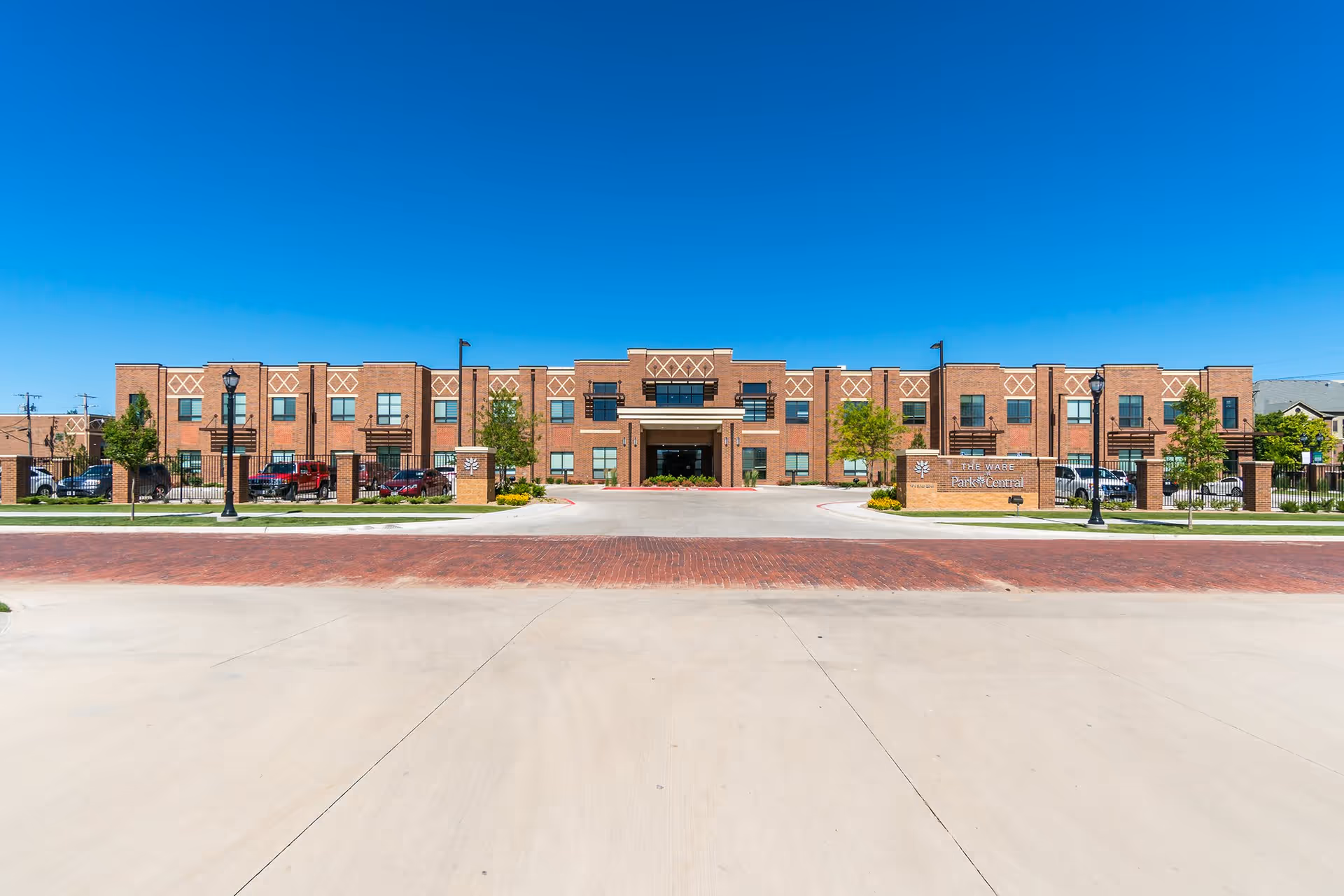 Front exterior view of Park Central Community building with a clear blue sky, brick facade, entrance driveway, and landscaped greenery.