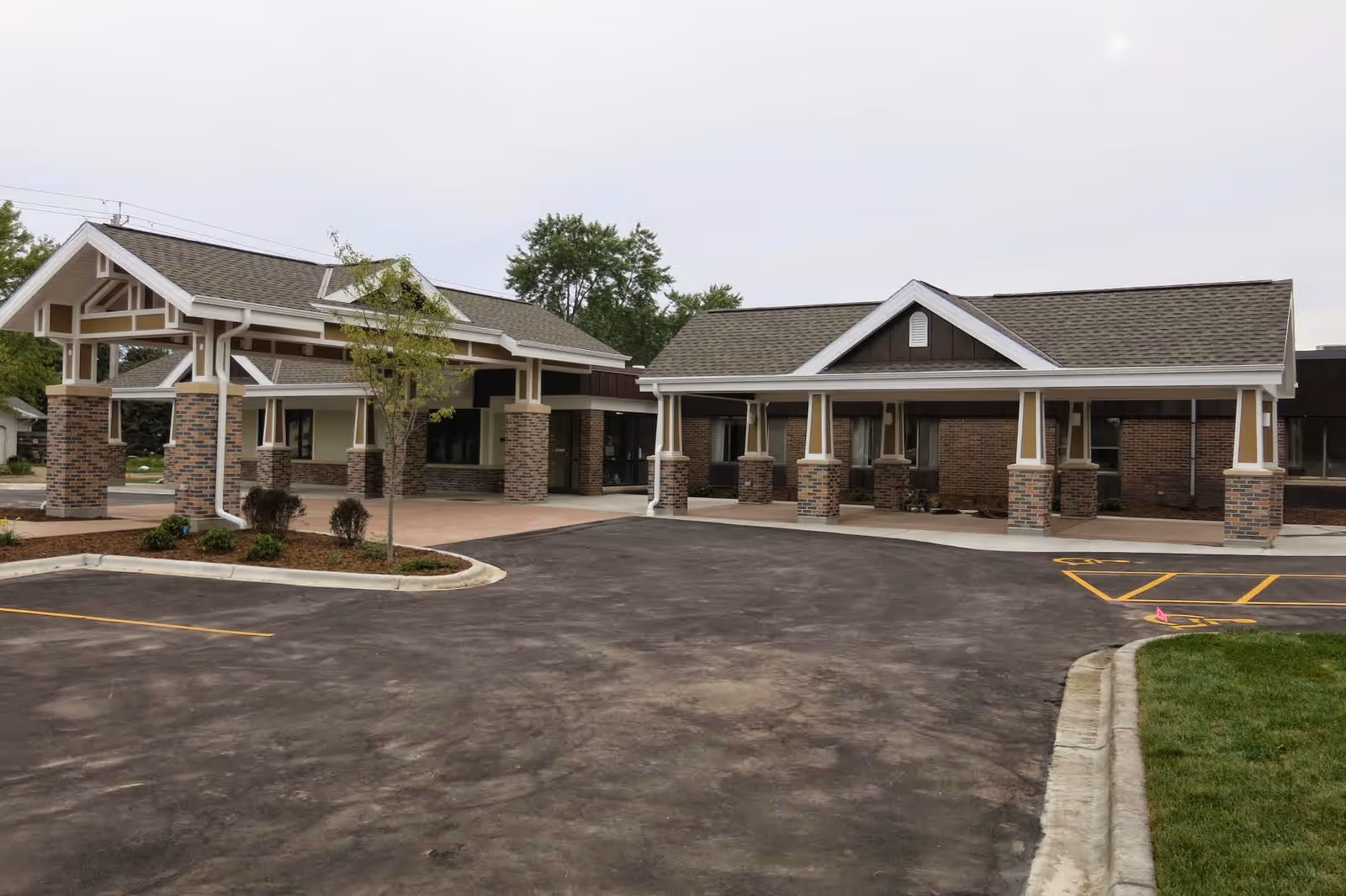 Covered main entrance and drive-up area of a single-story brick senior living facility with columns and parking.