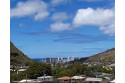 Hilly residential area with rooftops, trees, and a distant city skyline under blue sky.