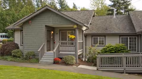 Gray lodge-style building with front entrance, steps, railing, and surrounding landscaping.