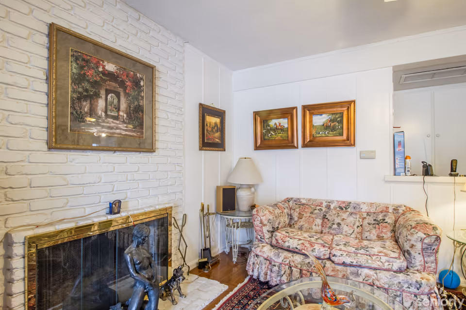 A cozy living room with floral couch, decorative paintings, and a fireplace.