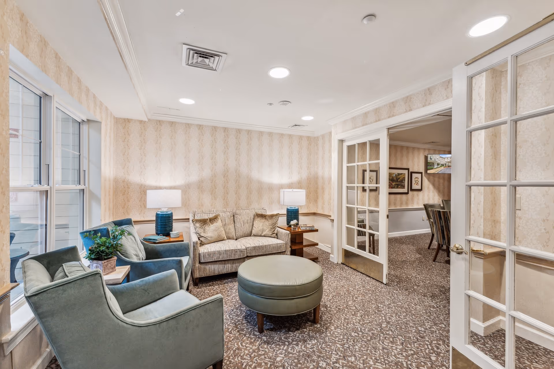 Cozy sitting area with armchairs, a sofa, an ottoman and side tables in a bright common room.