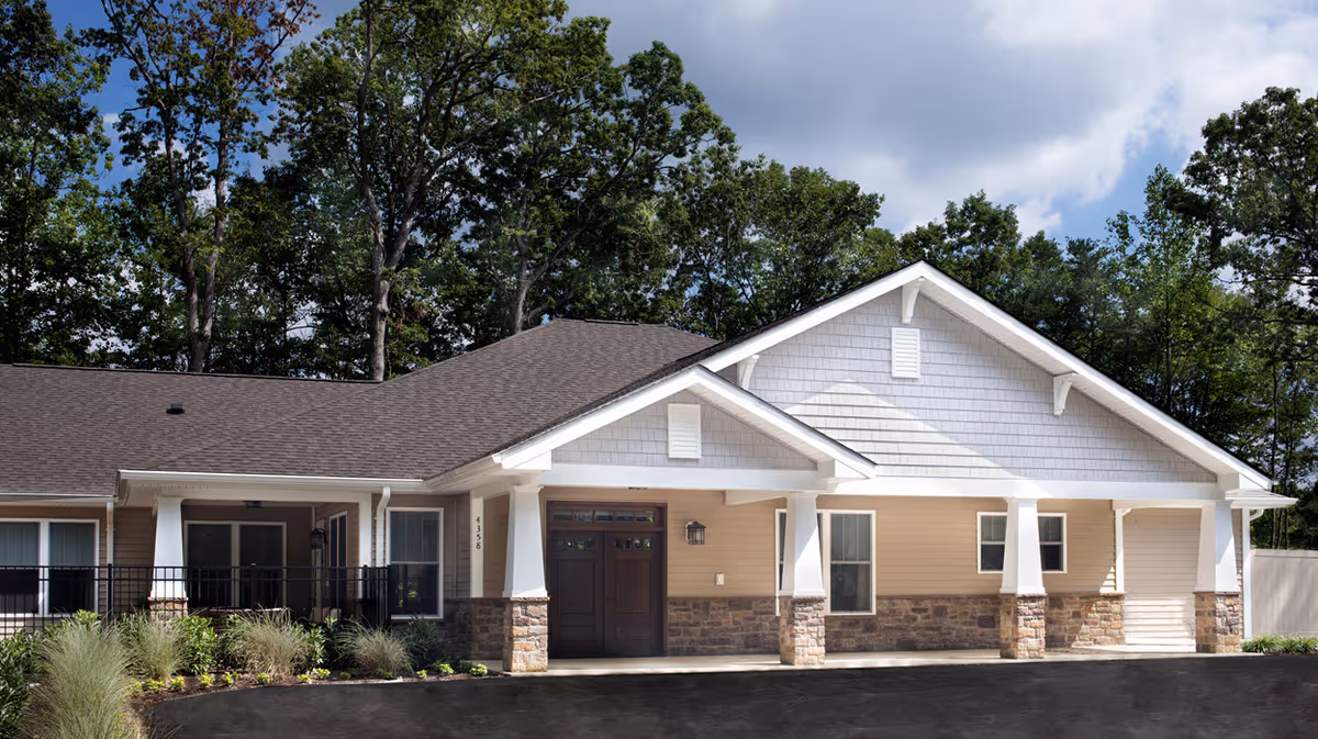 Front exterior of a single-story senior living building with a covered entrance, white columns, stone accents and trees in the background.
