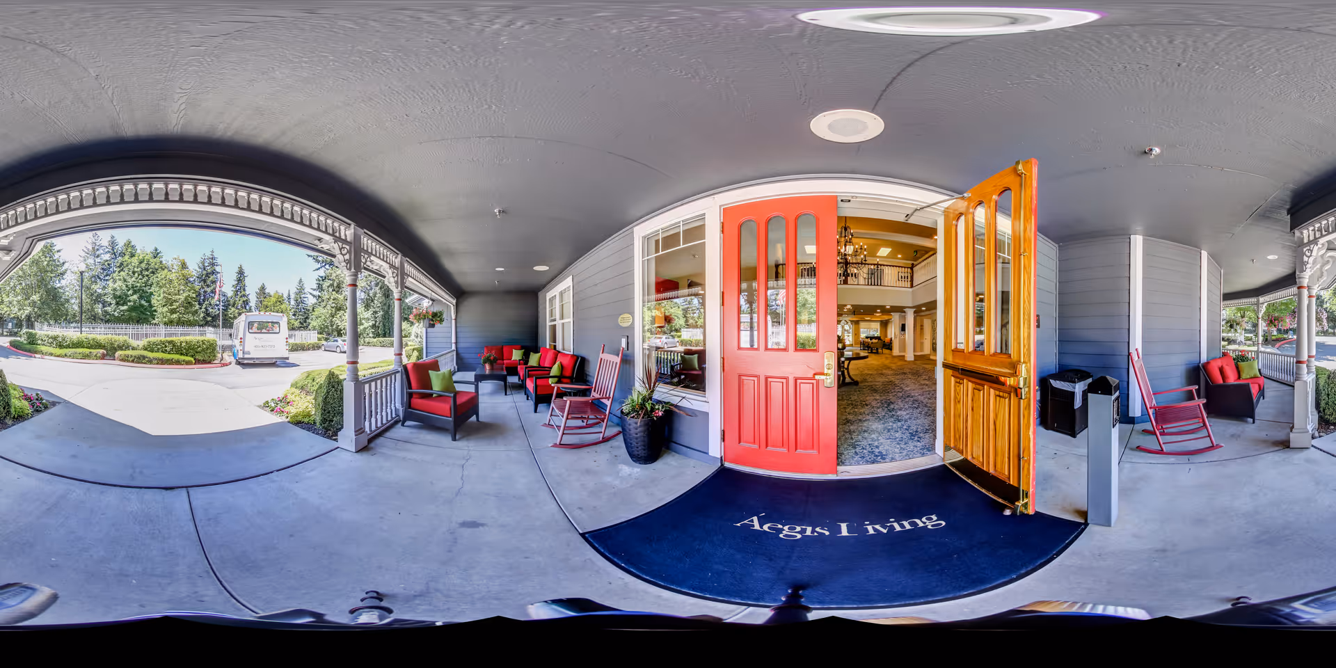 Covered front porch entrance of Aegis Living with open red doors, seating and rocking chairs overlooking the driveway.