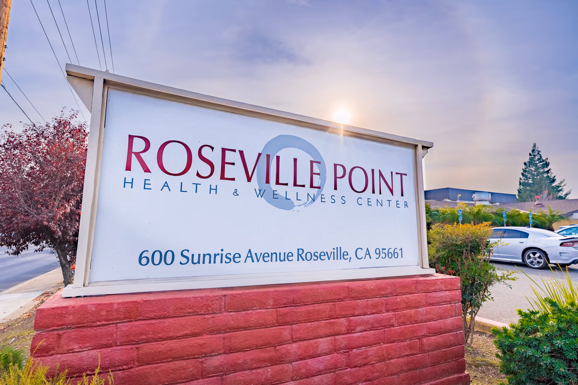 Outdoor sign reading 'Roseville Point Health & Wellness Center' with the address 600 Sunrise Avenue, Roseville, CA, mounted on a red brick base in front of the facility.