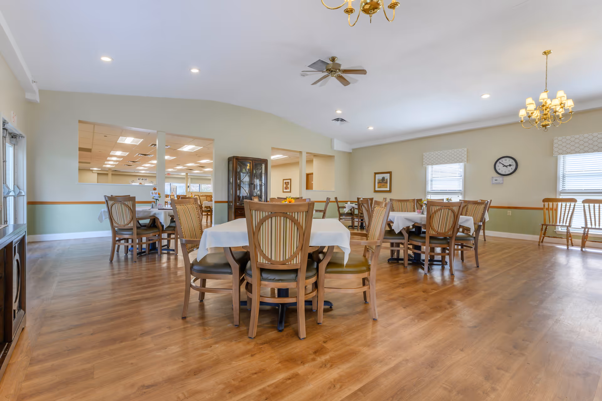 Spacious dining room with several tables covered in white tablecloths and wooden chairs on a hardwood floor.