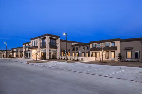 Exterior view of Sky Ridge senior living facility at dusk with parking lot and lit windows.