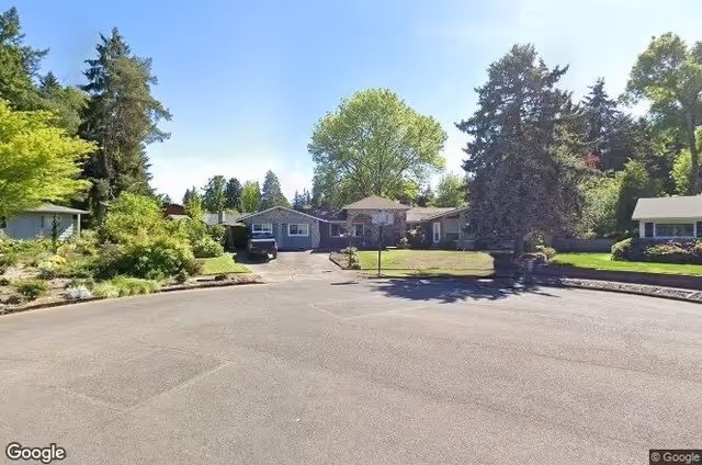 Single-story senior living facility with a driveway, trees, and a manicured lawn.