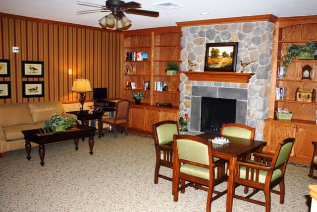 Cozy communal living room featuring a stone fireplace flanked by wooden built-in bookshelves, a seating area with a sofa and coffee table, and a card table with four chairs.