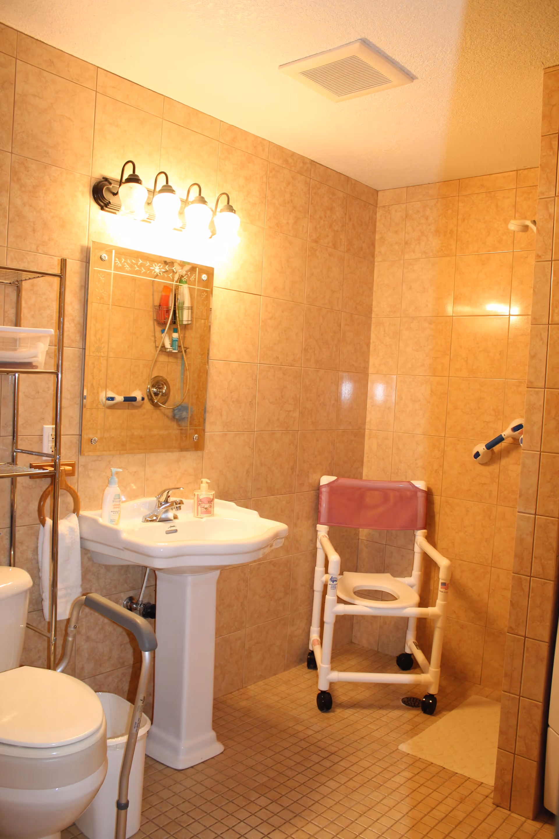 A bathroom featuring a sink, toilet, shower area, and a shower chair.