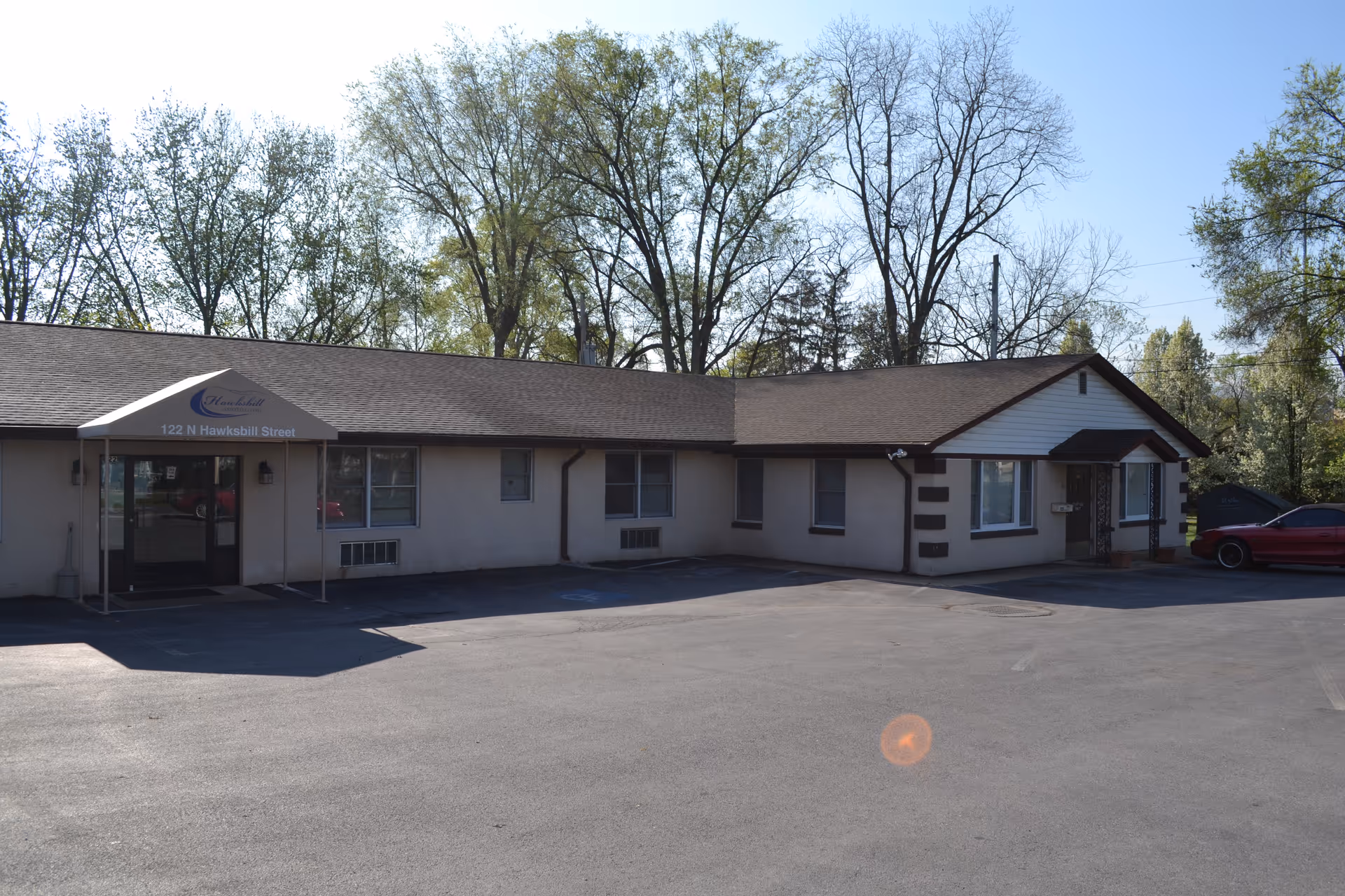 Front view of a single-story beige Hawksbill Assisted Living building with a parking lot.
