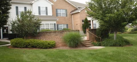 Two-story brick and siding senior living building with stairs, greenery, and a manicured lawn