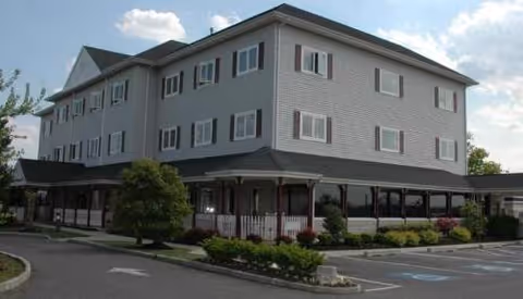 Exterior view of Bayside Manor, a gray three-story senior living building with a covered entrance.