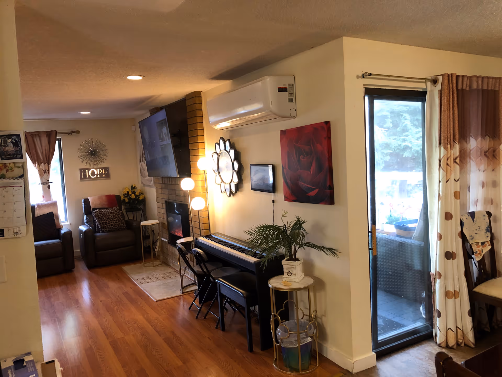Living room with two recliners by a fireplace and wall-mounted TV, a keyboard and decorative mirror on the wall, and a sliding glass door to a patio.