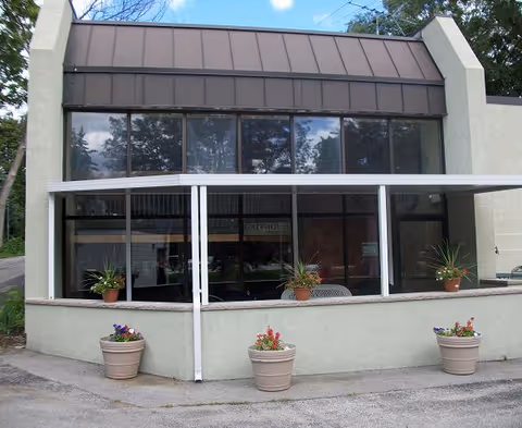 Facade of Gate House senior living entrance with large glass windows and potted plants.