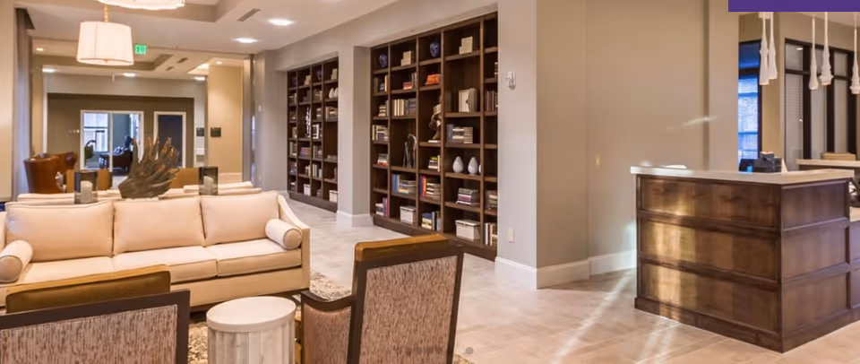 Spacious furnished lounge with sofas, chairs, a large bookshelf wall, and a reception desk.