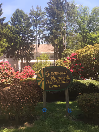 Outdoor sign for Greenwood Nursing & Rehabilitation Center among flowering shrubs.