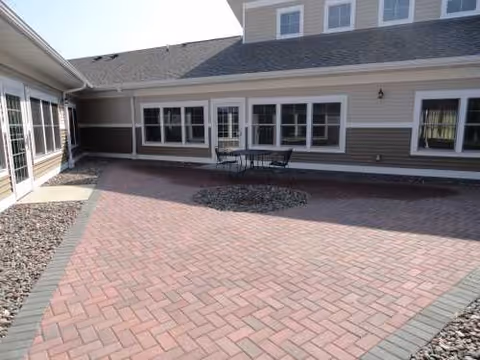 Brick-paved outdoor courtyard with a small table and chairs beside a beige building.