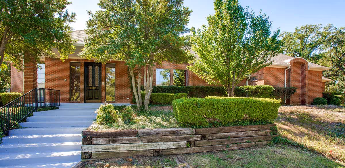 Avalon Memory Care entrance with brick facade, stairs, and landscaped trees