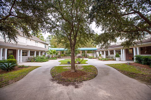 Exterior courtyard with a central tree, curved walkways and single-story residential buildings on either side.