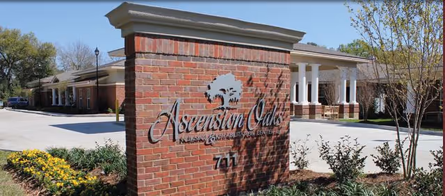Brick entrance sign reading 'Ascension Oaks Nursing and Rehabilitation Center' in front of a single-story brick building with columns and landscaping.