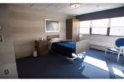 Sunlit private senior living bedroom with a single bed, nightstand, chair, and large window.