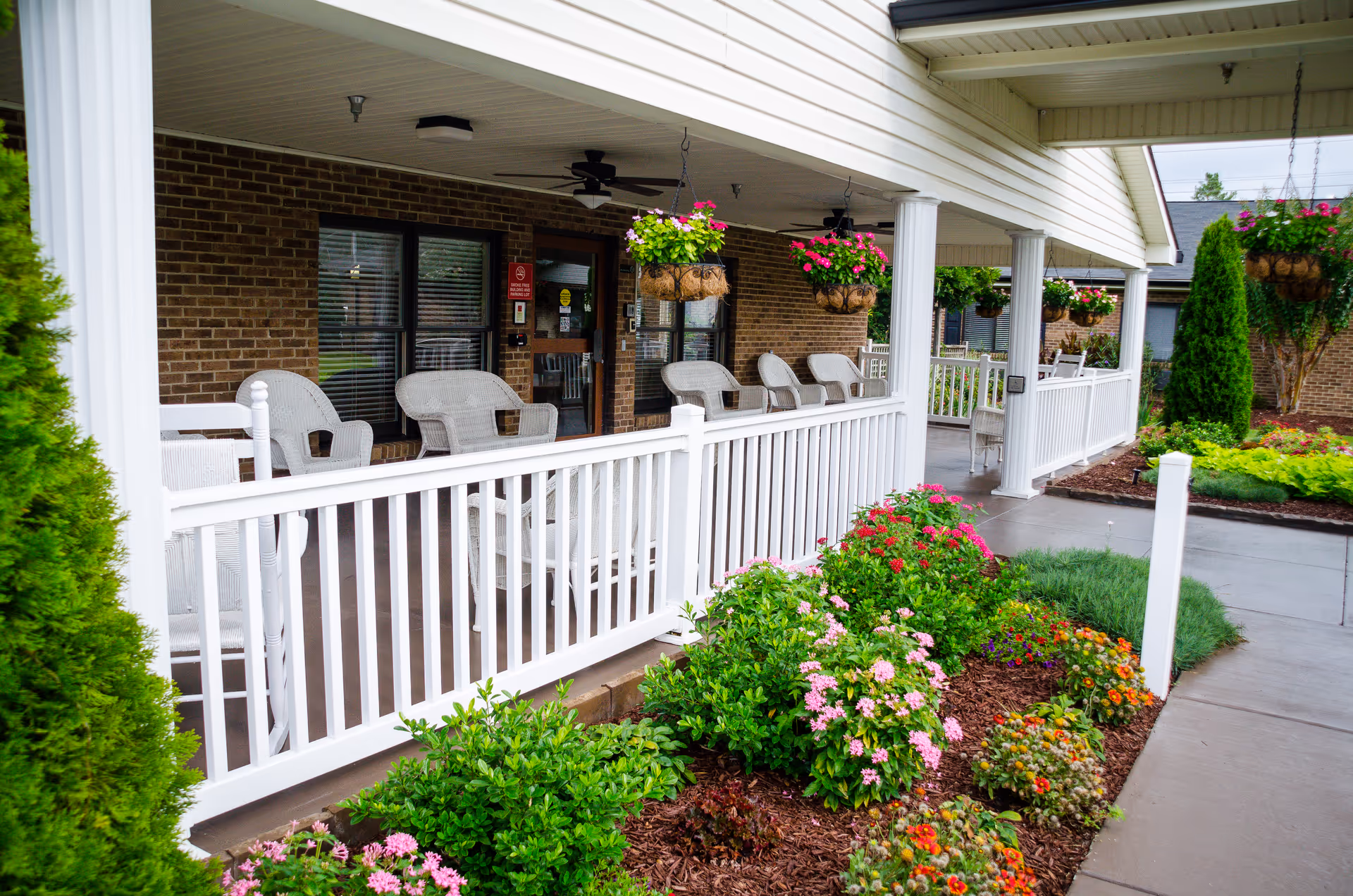 Bright brick building with a covered porch, white railing, and hanging flower baskets.