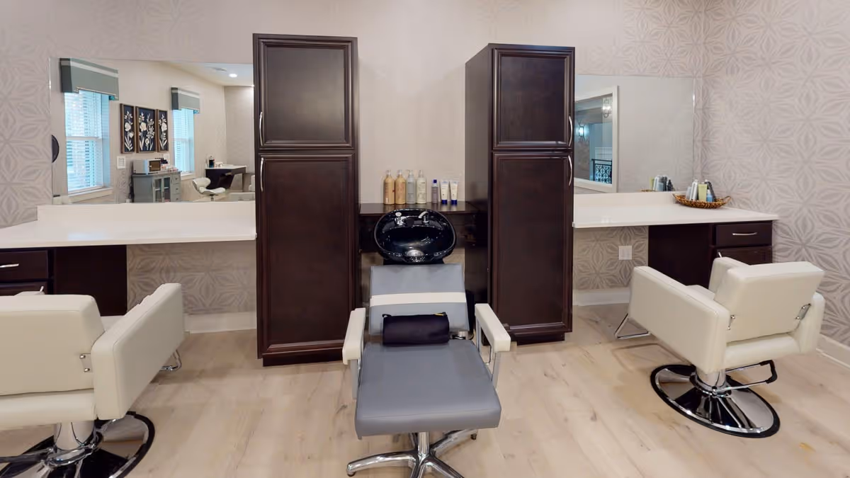 Interior salon area with three styling chairs, a central shampoo basin, mirrors, countertops, and dark storage cabinets.