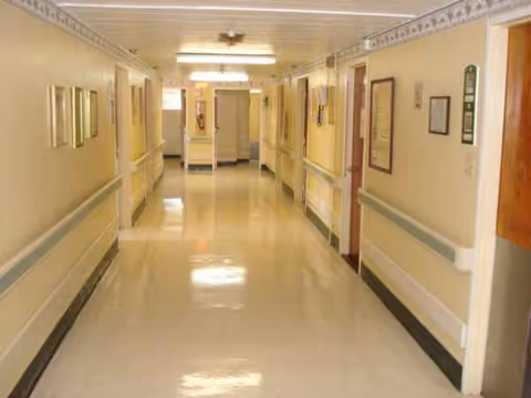Long well-lit corridor inside Marina Garden Nursing Center with beige walls and handrails.