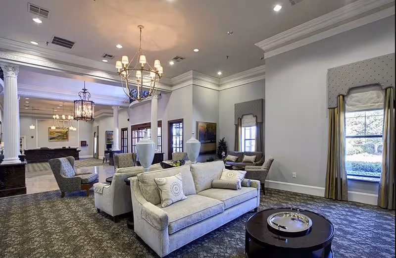 Spacious elegant lounge with sofas, armchairs, chandeliers, decorative columns, and large windows.