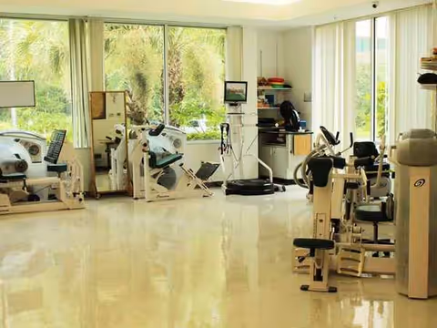 Bright rehabilitation gym with exercise equipment and large windows.