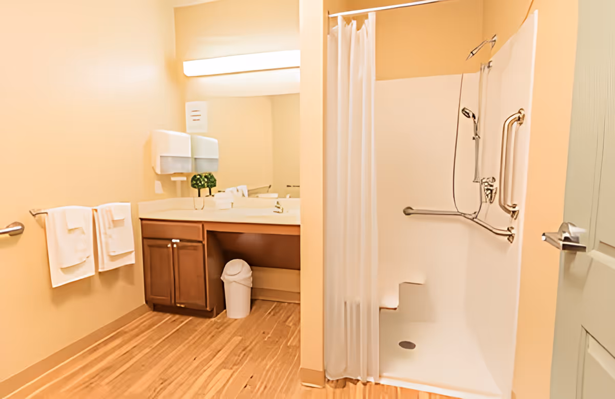 Accessible bathroom with a shower stall and grab bars, vanity with mirror, towel rack, and trash bin.