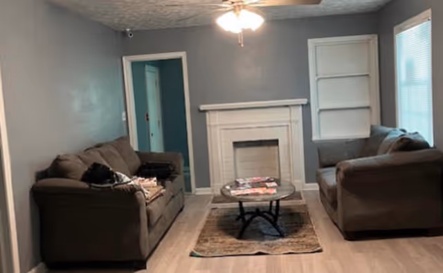 Living room with two sofas facing a white fireplace, a coffee table on a rug, and a ceiling fan overhead.
