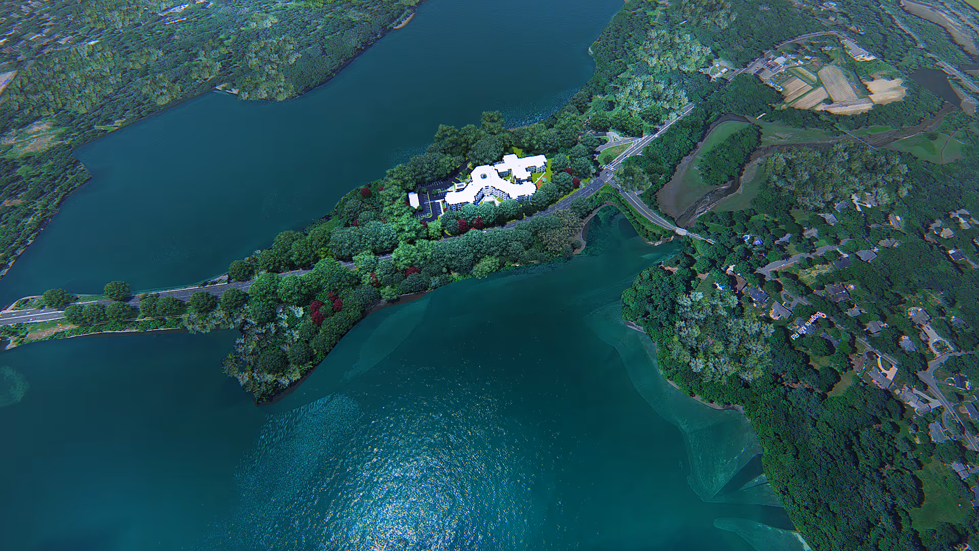Aerial view of a white building on a wooded peninsula surrounded by turquoise lakes and nearby homes.