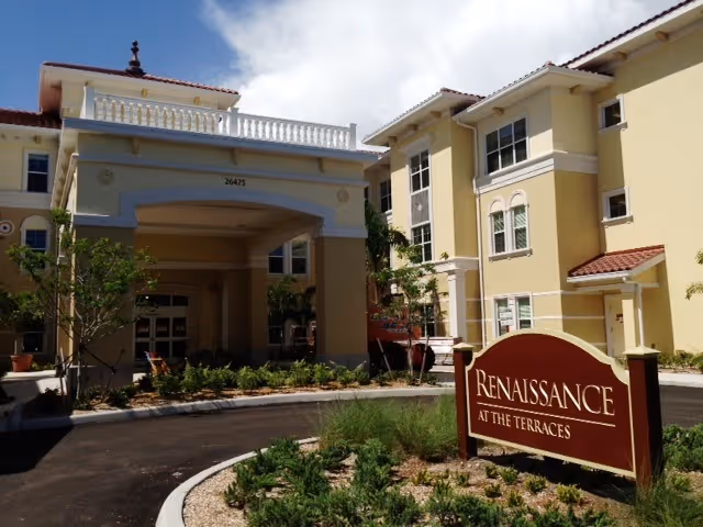 Exterior view of Renaissance at The Terraces senior living facility showing a multi-story beige building with a covered entrance and a landscaped driveway. A large sign with the facility name is visible in the foreground.