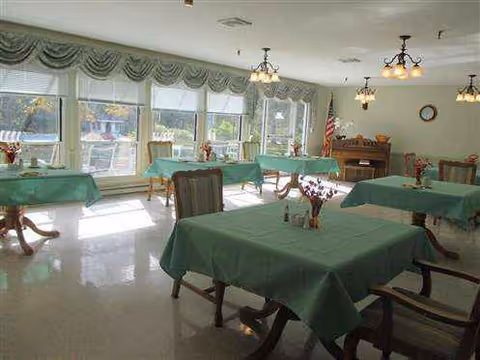 A bright dining room with green tablecloths on tables and wooden chairs.