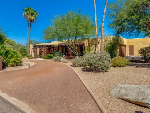 Desert landscaping frames a curved path to a ranch-style assisted living facility entrance.