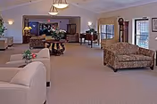 Spacious lounge with multiple sofas, armchairs, coffee tables, floral centerpieces, and large windows in a senior living facility.