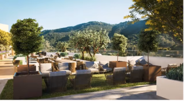 Outdoor terrace with lounge chairs and tables, potted trees, and mountains in the background.