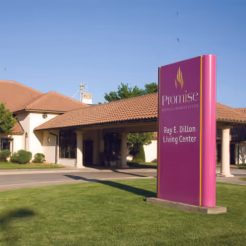 Front view of a senior living center with a purple sign and covered entrance.