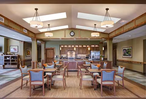 Empty dining room with wooden tables and cushioned chairs, warm lighting.